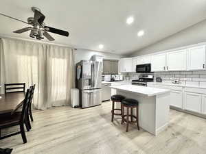 Kitchen with stainless steel appliances, light wood finished floors, a kitchen island, light countertops, and white cabinetry