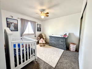 Bedroom featuring dark colored carpet, a textured ceiling, a nursery area, and ceiling fan