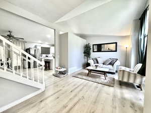 Living room with light wood-style floors, lofted ceiling, a ceiling fan, baseboards, and stairway