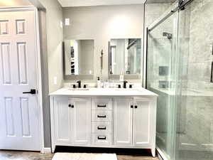 Full bathroom featuring a shower stall, double vanity, and wood finished floors