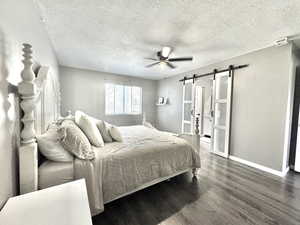 Bedroom with a barn door, wood finished floors, baseboards, a textured ceiling, and a ceiling fan
