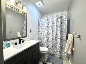 Full bathroom featuring vanity, toilet, a textured ceiling, a shower with shower curtain, and tile patterned flooring
