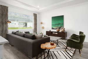 Living room featuring wood finished floors, recessed lighting, a tray ceiling, and baseboards