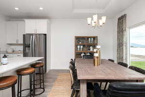 Dining room with wood finished floors, a chandelier, recessed lighting, a raised ceiling, and baseboards
