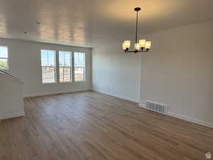 Spare room featuring wood finished floors, a chandelier, and baseboards