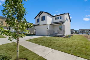 View of front of house with stucco siding, a garage, concrete driveway, a front yard, and stone siding