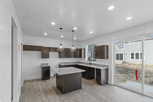 Kitchen with dark brown cabinets, a kitchen island, a sink, recessed lighting, and light wood finished floors