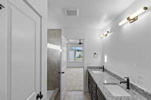 Primary bathroom with double vanity, tile patterned flooring, tiled shower, and baseboards