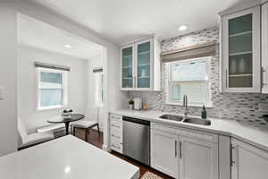 Kitchen featuring stainless steel dishwasher, a sink, light countertops, decorative backsplash, and recessed lighting
