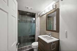 Bathroom featuring tile walls, toilet, a shower stall, vanity, and decorative backsplash
