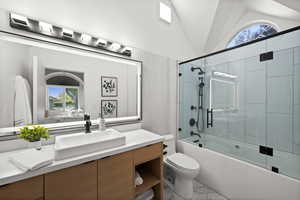 Bathroom with vanity, toilet, bath / shower combo with glass door, and lofted ceiling