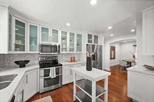 Kitchen featuring stainless steel appliances, arched walkways, backsplash, white cabinetry, and dark wood-style floors