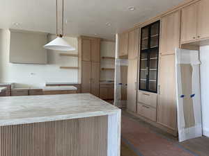 Kitchen featuring light brown cabinets, decorative light fixtures, glass insert cabinets, recessed lighting, and light stone countertops