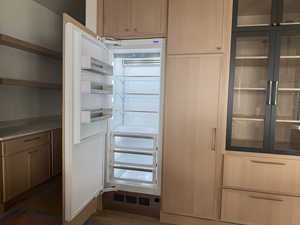 Kitchen featuring light brown cabinetry, glass insert cabinets, paneled refrigerator, and dark wood-style flooring