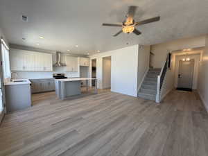 Kitchen with wall chimney exhaust hood, a sink, light wood-style flooring, a center island, and a textured ceiling