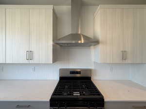 Kitchen featuring wall chimney range hood, stainless steel range with gas stovetop, backsplash, and light stone counters