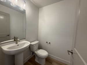 Half bathroom with toilet, baseboards, wood finished floors, and a sink