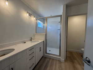 Full bath with wood finished floors, a shower stall, toilet, a textured ceiling, and double vanity