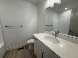 Full bathroom with wood finished floors, toilet, vanity, baseboards, and a shower