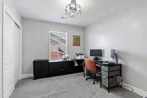 Carpeted home office/bedroom featuring baseboards and a chandelier