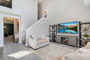 Living area featuring a glass covered fireplace, a towering ceiling, stairs, wood finished floors, and baseboards