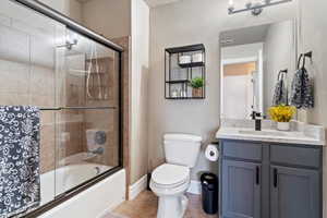 Bathroom featuring toilet, vanity, tile patterned flooring, bath / shower combo with glass door, and baseboards