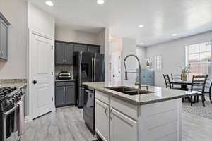 Kitchen with a sink, stainless steel appliances, light wood-type flooring, light stone countertops, and backsplash