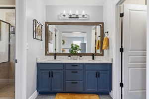 Full bathroom featuring a shower stall, double vanity, and baseboards
