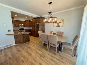 Dining room with ornamental molding, light wood finished floors, a chandelier, recessed lighting, and baseboards