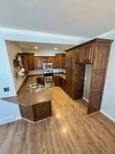 Kitchen with appliances with stainless steel finishes, a peninsula, a sink, crown molding, and dark countertops
