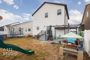 Rear view of property featuring a trampoline, stucco siding, a pergola, and a playground