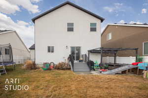 Back of house featuring a trampoline, stucco siding, a pergola, and a patio area