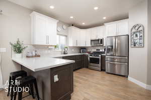 Kitchen featuring appliances with stainless steel finishes, a peninsula, white cabinets, a kitchen bar, and recessed lighting