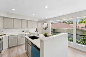 Kitchen with dishwashing machine, a sink, light wood-style floors, gray cabinets, and recessed lighting