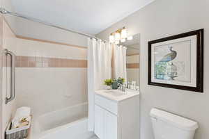 Bathroom featuring vanity, shower / bathtub combination with curtain, and toilet