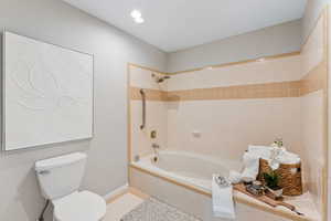Bathroom featuring toilet, tiled shower / bath, tile patterned floors, and baseboards