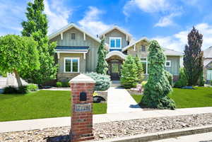 Craftsman-style home featuring board and batten siding, a front yard, stone siding, and a standing seam roof