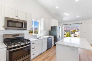 Kitchen with stainless steel appliances, a kitchen island, lofted ceiling, backsplash, and light countertops