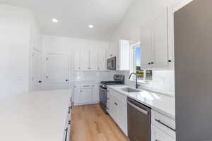 Kitchen with appliances with stainless steel finishes, a sink, backsplash, light wood finished floors, and white cabinets
