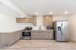 Basement kitchen featuring stainless steel appliances, light wood-style flooring, recessed lighting, light countertops, and a sink