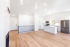 Kitchen with appliances with stainless steel finishes, a kitchen island, white cabinetry, a sink, and vaulted ceiling