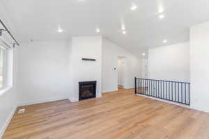 Unfurnished living room with light wood-style floors, recessed lighting, baseboards, a glass covered fireplace, and vaulted ceiling
