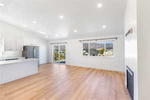 Unfurnished living room with vaulted ceiling, light wood-style floors, recessed lighting, and baseboards