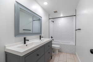 Bathroom with double vanity, toilet, tiled shower / bath combo, and recessed lighting