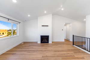 Unfurnished living room featuring vaulted ceiling, a fireplace, recessed lighting, baseboards, and light wood-style floors