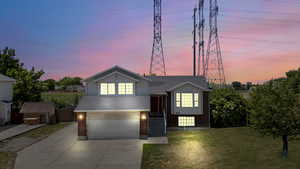 Tri-level home with brick siding, an attached garage, concrete driveway, a lawn, and a shingled roof