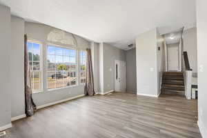 Unfurnished living room featuring a textured ceiling, light wood-style flooring, stairs, baseboards, and lofted ceiling