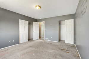 Unfurnished bedroom featuring two closets, baseboards, carpet floors, and a textured ceiling