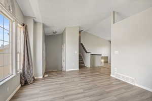 Unfurnished room featuring light wood-type flooring, stairs, baseboards, lofted ceiling, and a textured ceiling