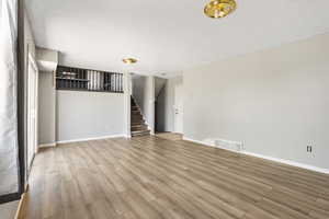 Unfurnished living room featuring wood finished floors, stairway, a textured ceiling, and baseboards